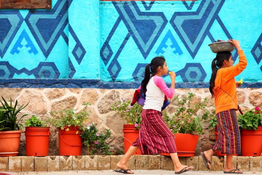 Niñas mayas caminando junto a murales geométricos azules