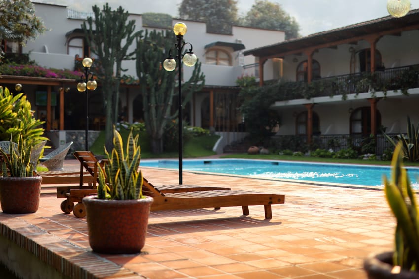 Piscina de día con lettini, palme y faroles