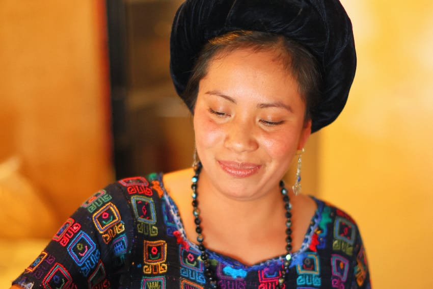 Mujer maya sonriente con tocado de tela y huipil bordado